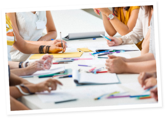 Image of people at desk with pens and paper 